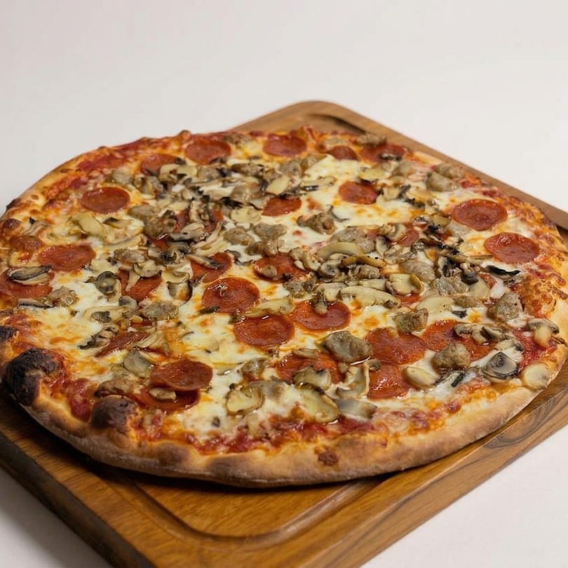 A whole pepperoni, mushroom, and sausage pizza on a wooden serving board.