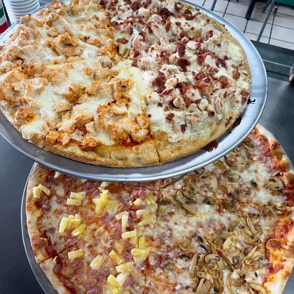 Two multi-topping pizzas, one with chicken and bacon, the other with pineapple and mushrooms.