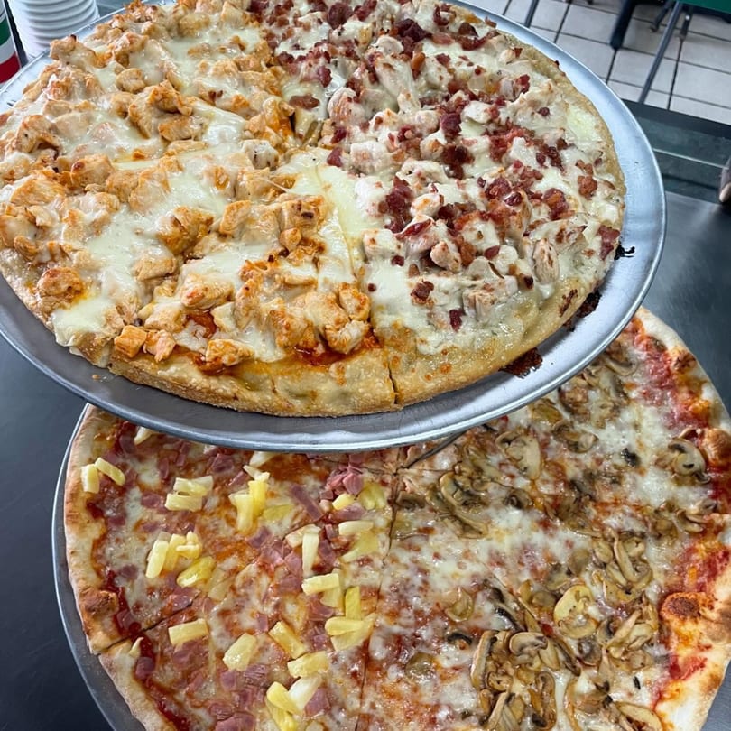 Two multi-topping pizzas, one with chicken and bacon, the other with pineapple and mushrooms.